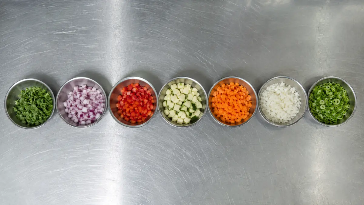Hilera de bowls metálicos con ingredientes picados sobre una mesada
