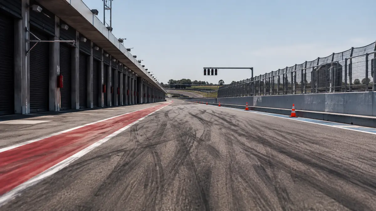 Calle de boxes de un autodromo con asfalto marcado, conos y el semaforo de pista al fondo
