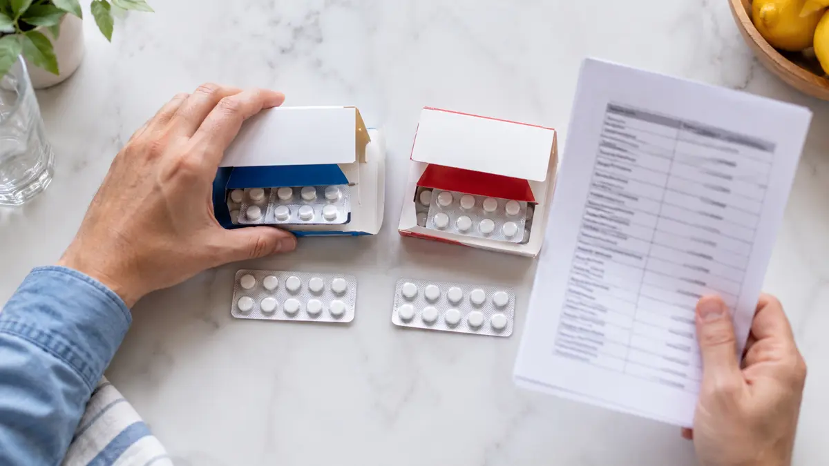 Dos cajas genéricas con comprimidos iguales mientras una mano evita mezclarlos y revisa los principios activos